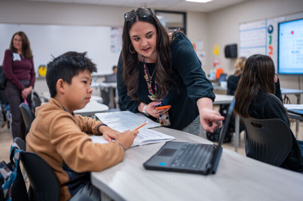 A teacher standing next to a student at his desk