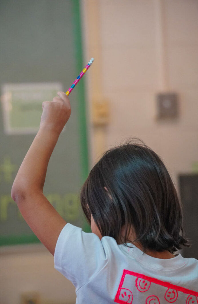 A student with their hand raised in the air, holding a pencil