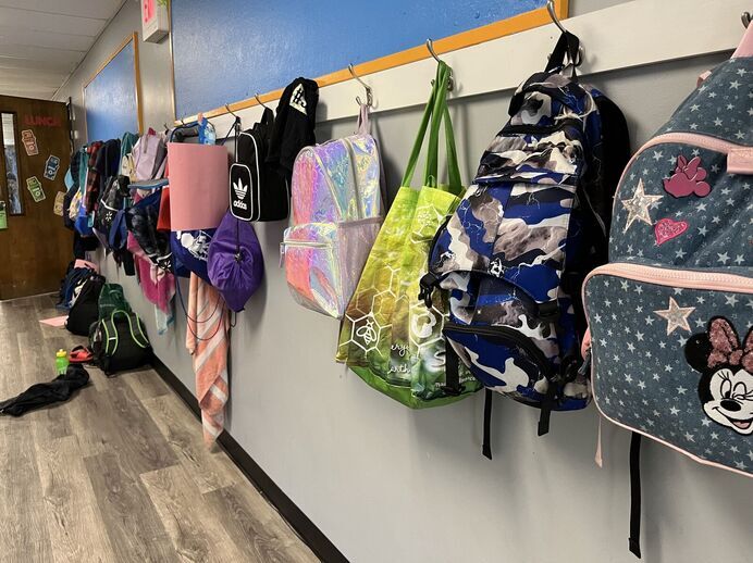 A school hallway with different colored backpacks lined against the walls