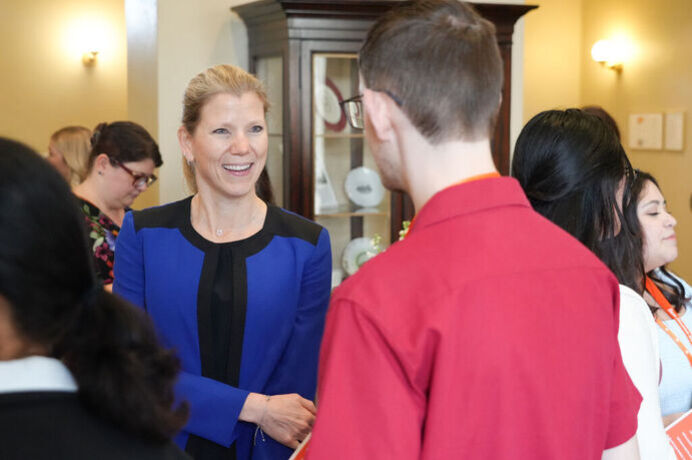 Stacey smiling while in conversation with an individual with his back turned towards the camera